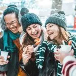 Glade venner drikker gløgg og varm chokolade på julemarked - Glade unge mennesker nyder vinterferien på weekendophold - Fokus på asiatisk fyr