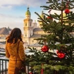 Ung kvinne sett bakfra står på bakgrunn av solfylt jul i Salzburg, Østerrike. Juletrær med røde julekuler på bakgrunn av vinteren i Salzburg.