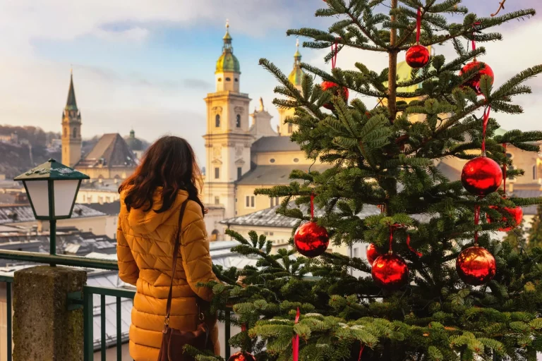 Young woman view from the back stands on the background of sunny Christmas Salzburg, Austria. Christmas trees with red Christmas balls against the background of the winter Salzburg.